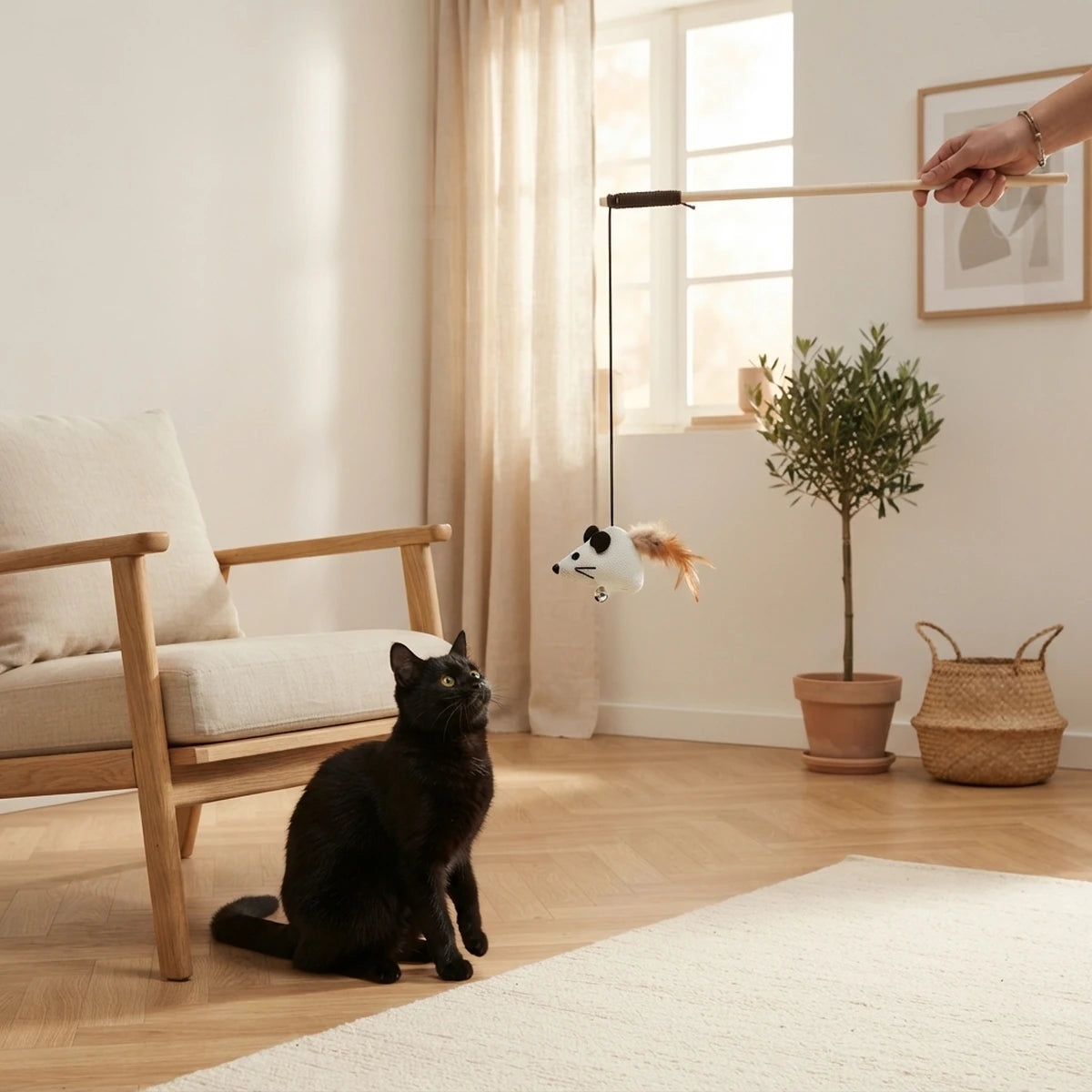 Baguette pour chat La Frimousse tenue à la main dans un salon, chat noir prêt à bondir